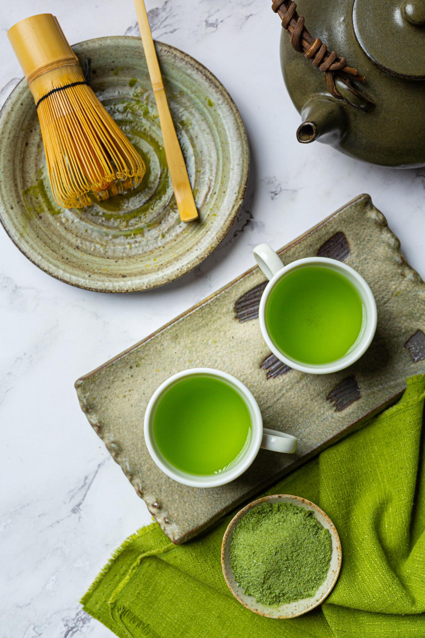 Hot green tea in a glass with cream topped with green tea, decorated with green tea powder.